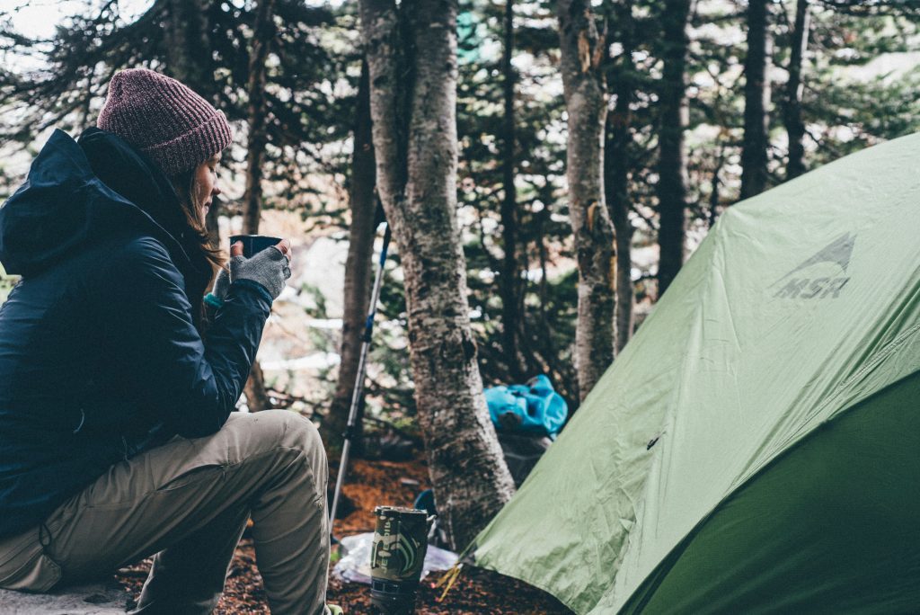 Woman sitting by her tent drinking some coffe and enjoying the benefits of camping